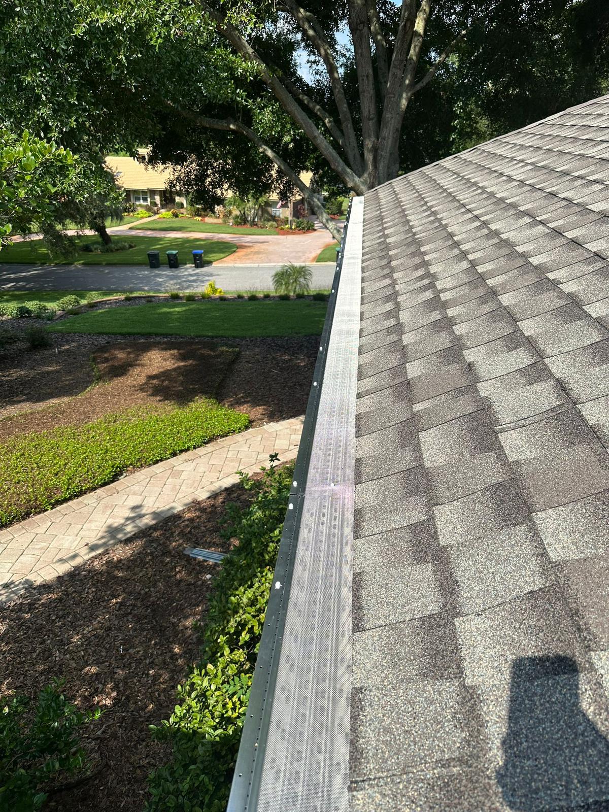 Perforated metal gutter guard installed on a dark gutter at the edge of a shingle roof